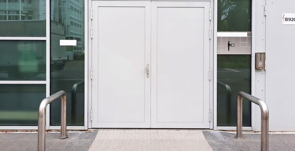 Grey double service doors set in a panelled facade, a small access reader mounted on the pillar to their right