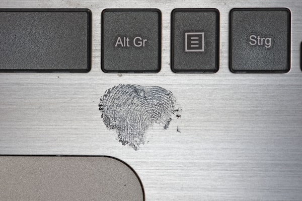 A latent fingerprint dusted in grey powder on the brushed-metal deck of a laptop, below keys marked Alt Gr and Strg
